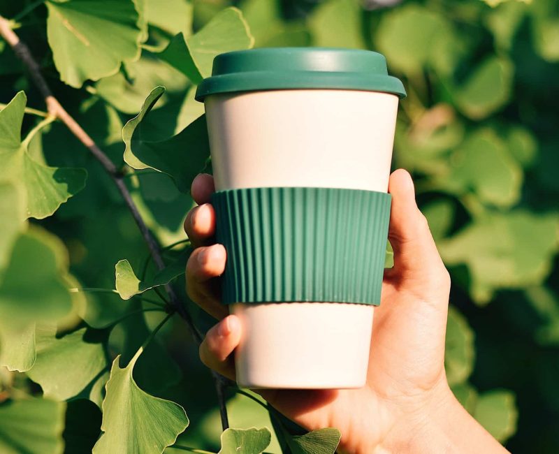 hand-holding-eco-friendly-reusable-coffee-cup-against-green-background.jpg